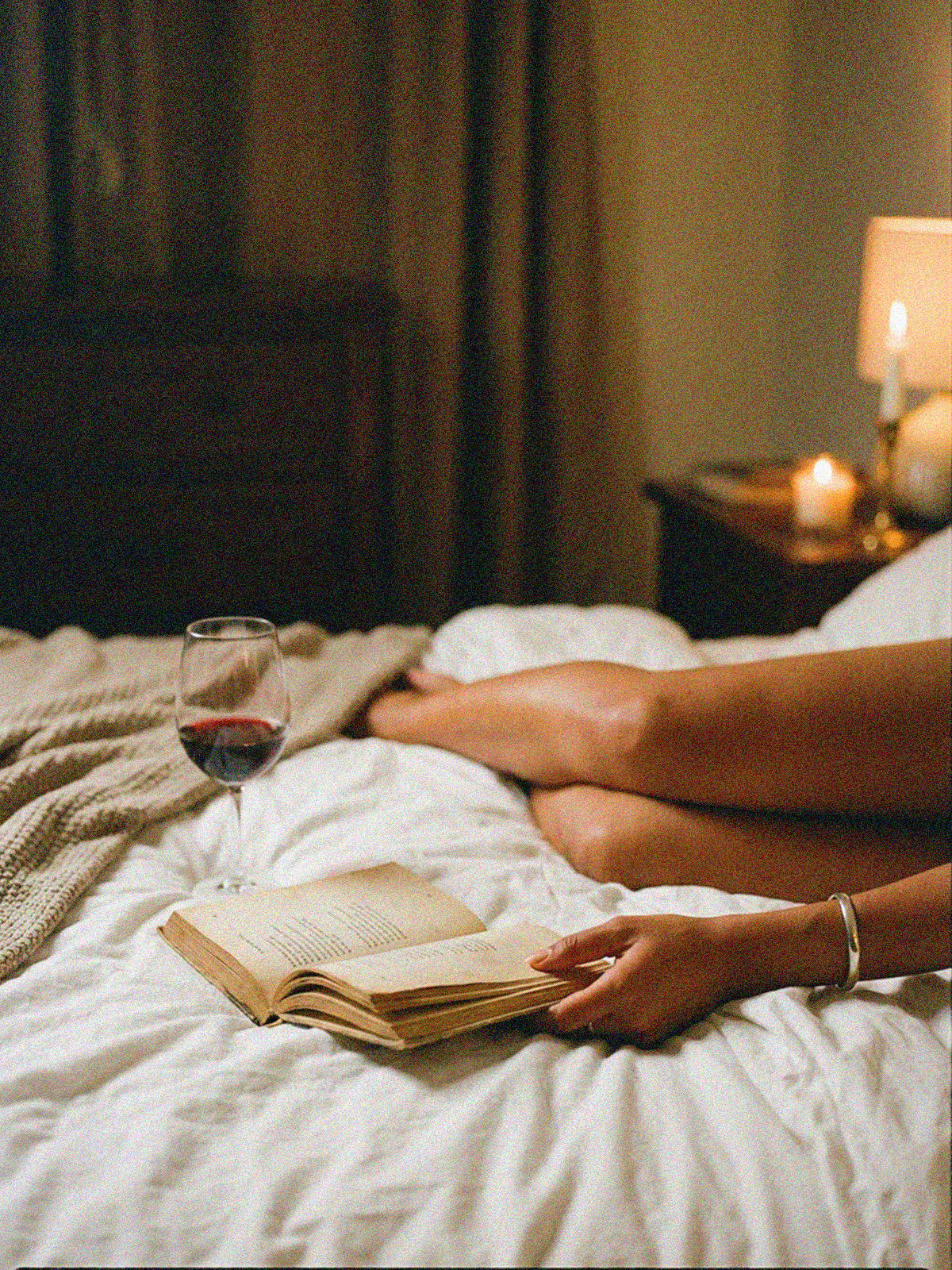 Un libro abierto y una copa de vino sobre la cama, a la luz de una vela